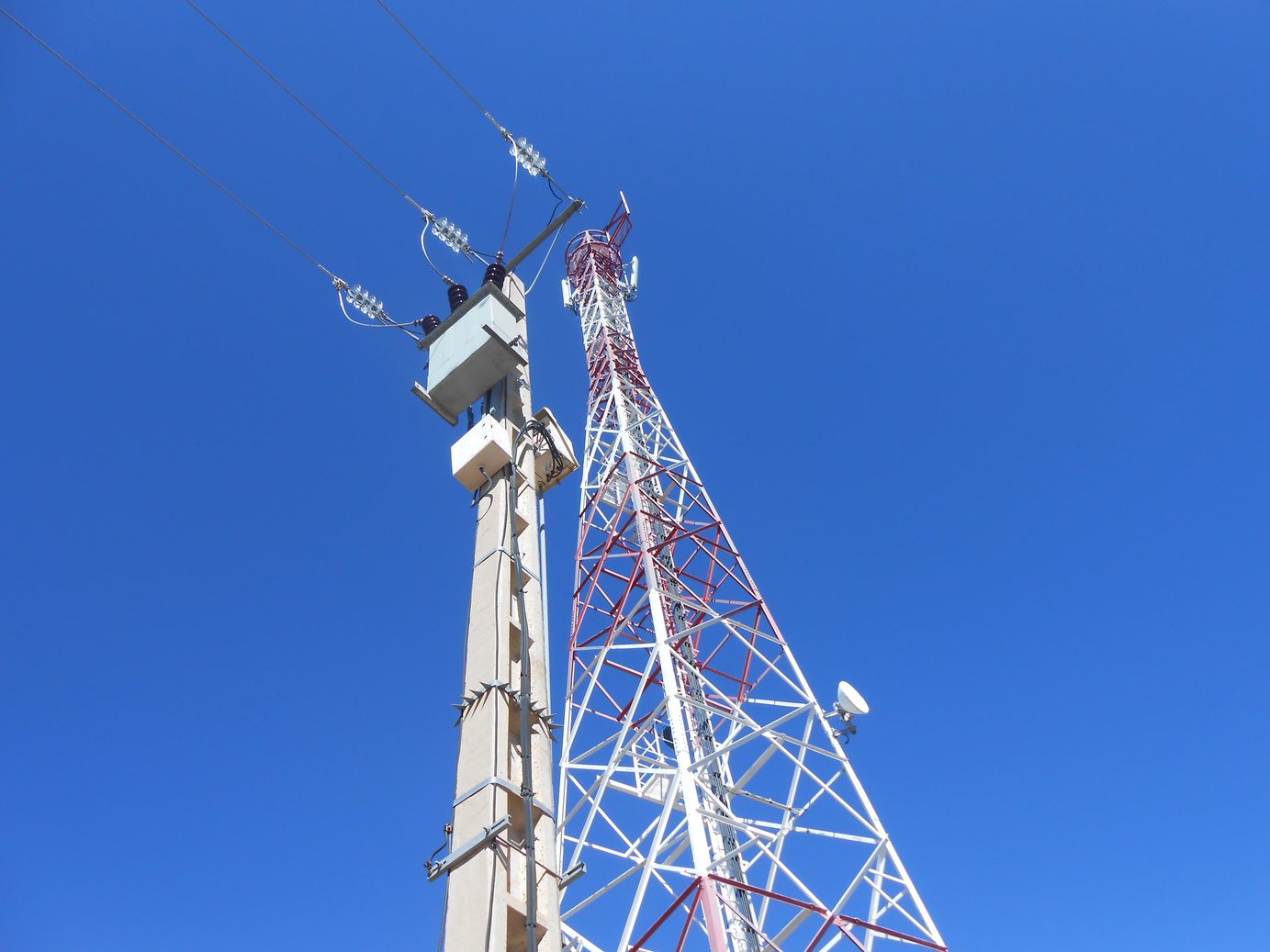 Red and white telecom tower beside a utility pole